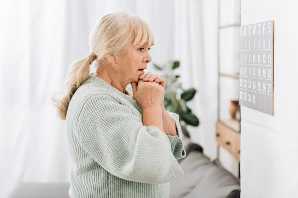 Upset senior woman touching head and looking at wall calendar — Stock Photo