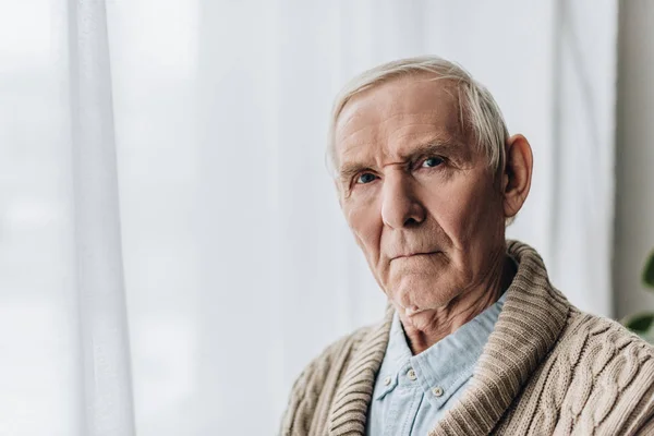 Расстроенный пенсионер с седыми волосами, смотрящий в камеру — стоковое фото