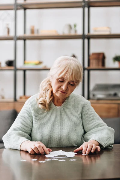 Rentnerin betrachtet Puzzleteile auf Tisch — Stock Photo