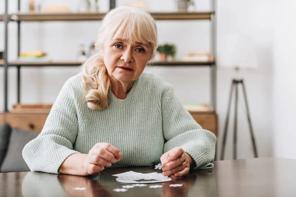 Senior woman holding jigsaw piece while playing with puzzles — Stock Photo