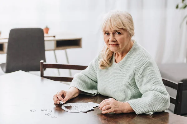 Blonde retired woman playing with puzzles at home — Stock Photo