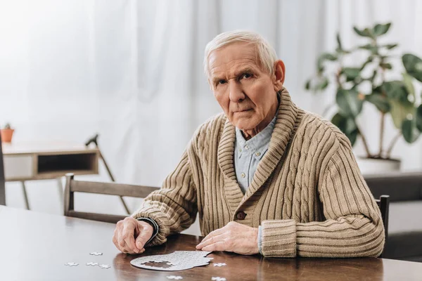 Pensionato triste con i capelli grigi che gioca con i puzzle a casa — Foto stock