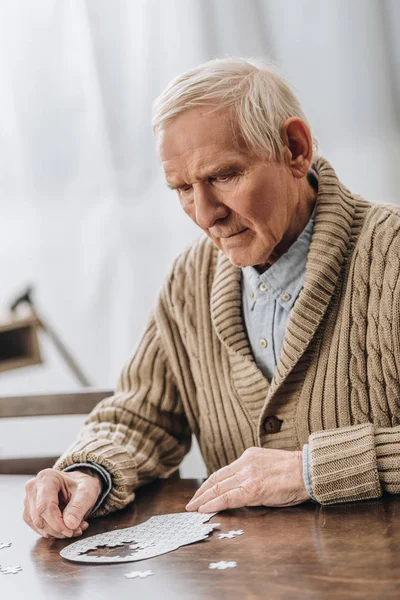 Triste hombre retirado con el pelo gris jugando con rompecabezas en casa - foto de stock