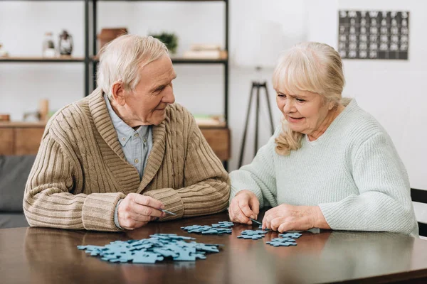 Feliz pareja jubilada jugando con rompecabezas en casa - foto de stock