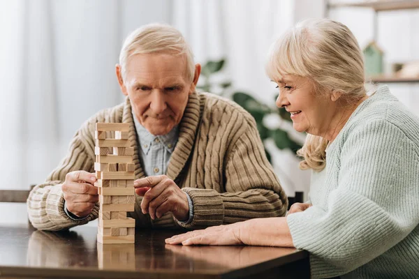 Marido y mujer jubilados jugando jenga juego en la mesa - foto de stock