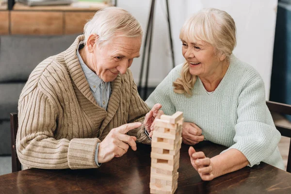 Fröhliche Rentner Mann und Frau spielen Jenga-Spiel auf dem Tisch — Stockfoto