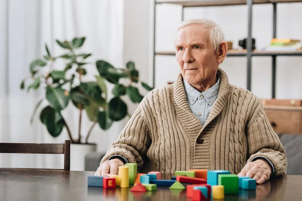Hombre mayor sentado cerca de juguetes de madera en casa - foto de stock