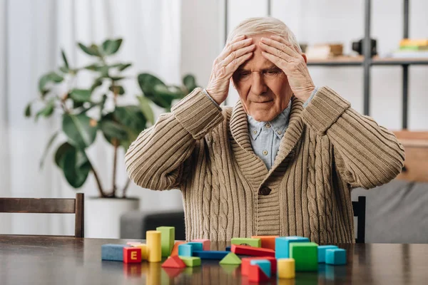 Rentner hat Kopfschmerzen, wenn er zu Hause neben Holzspielzeug sitzt — Stockfoto