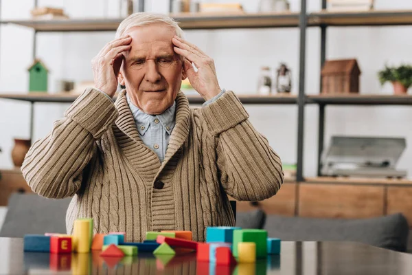 Pensioner having headache while sitting near wooden toys — Stock Photo