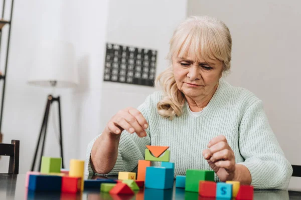 Blonde Rentnerin spielt zu Hause mit Holzspielzeug — Stock Photo