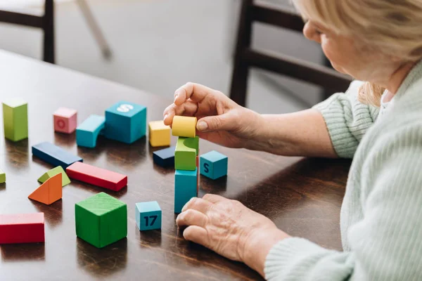 Senior woman playing with wooden cubes on table — Stock Photo