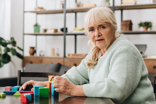 Blonde senior woman sitting near wooden toys at home — Stock Photo