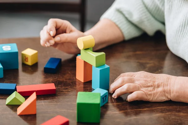 Vista recortada de la mujer mayor jugando con juguetes de madera en la mesa - foto de stock