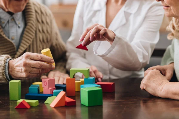 Vue recadrée du couple retraité et de l'aidant jouant avec des jouets en bois — Photo de stock