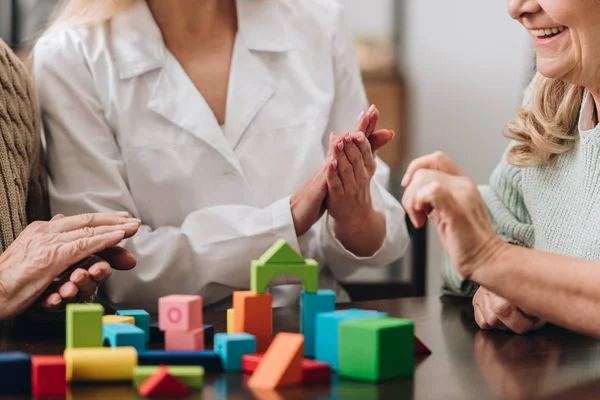 Vue recadrée de soignant applaudissant au couple aîné tout en jouant avec des jouets en bois — Photo de stock