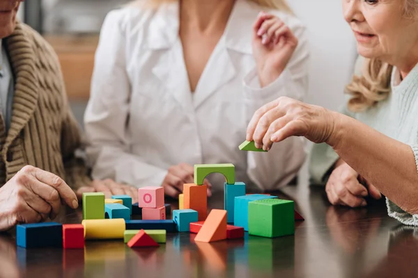 Vue recadrée de la femme assise avec un couple retraité et jouant avec des jouets en bois — Photo de stock