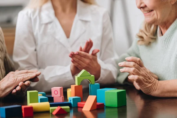 Cropped view of caregiver applauding to retired couple while playing with wooden toys — Stock Photo