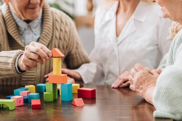 Vue recadrée de l'aidant assis avec l'homme et la femme à la retraite et jouant avec des jouets en bois — Photo de stock