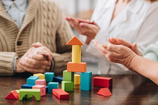 Vista recortada del cuidador sentado con pensionistas jubilados y jugando cerca de juguetes de madera - foto de stock