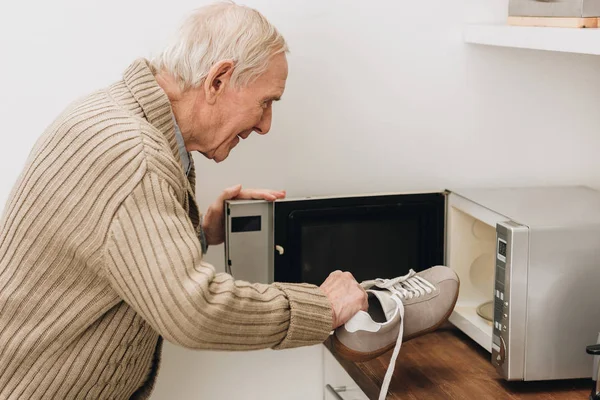 Retired man with dementia disease putting shoe in microwave oven — Stock Photo