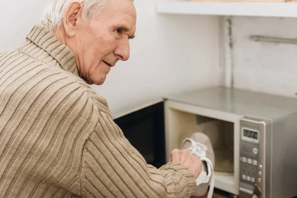 Senior man with dementia disease putting shoe in microwave oven — Stock Photo