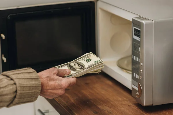 Vista recortada del hombre mayor poniendo dinero en el horno de microondas - foto de stock