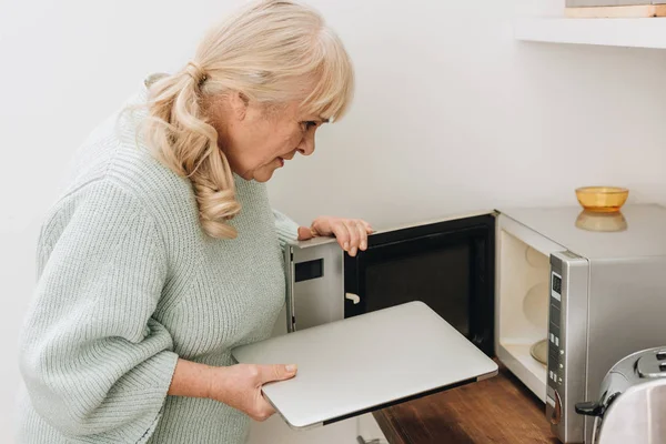 Mujer mayor con demencia poner portátil en el horno de microondas — Stock Photo