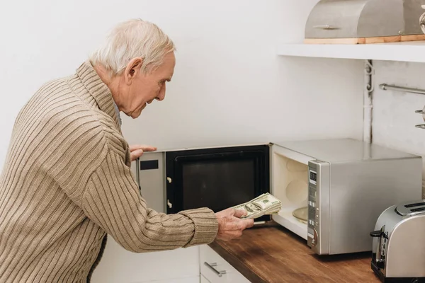 Hombre mayor con demencia poniendo dólares en el horno de microondas - foto de stock