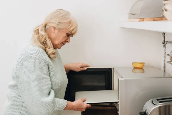 Retired woman with dementia disease putting laptop in microwave oven — Stock Photo