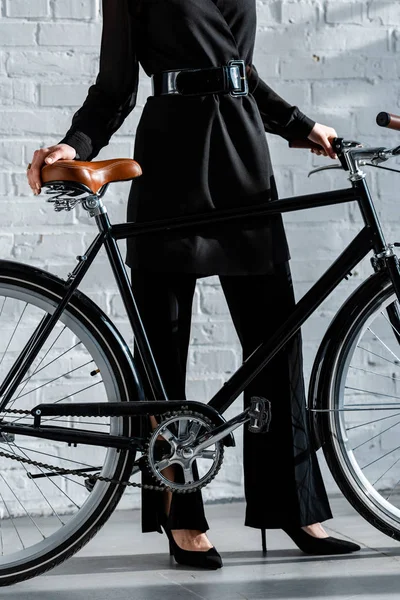 Femme en vêtements noirs tenant vélo noir — Photo de stock