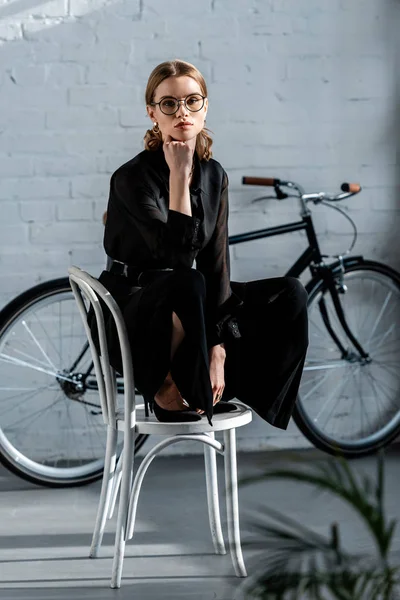 Attractive woman in black clothes sitting on chair and looking at camera — Stock Photo