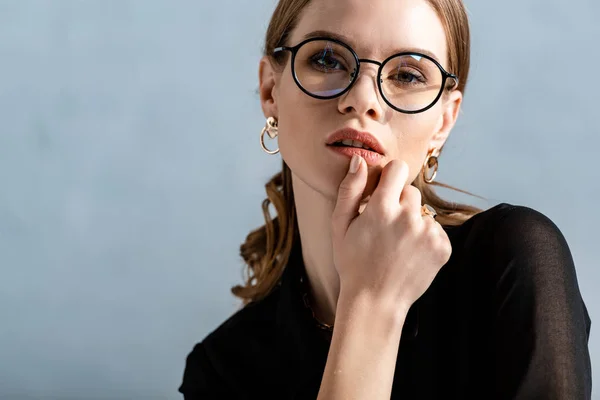 Séduisante femme en vêtements noirs regardant caméra et lèvres touchantes — Photo de stock