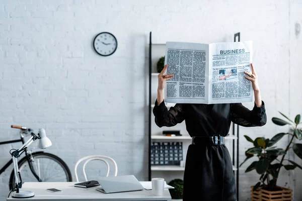 Mujer de negocios en ropa negra sosteniendo periódico en frente de la cara - foto de stock