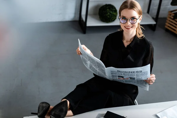 Belle femme d'affaires en vêtements noirs et lunettes assis à la table et souriant à la caméra — Photo de stock