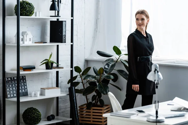 Красивая улыбающаяся женщина в черной одежде позирует в офисе — стоковое фото
