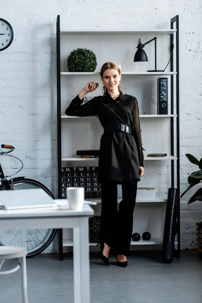 Улыбающаяся деловая женщина в черной формальной одежде в современном офисе — стоковое фото
