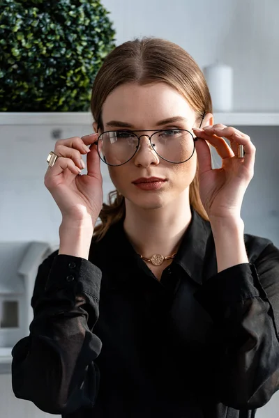 Portrait of beautiful woman in black putting on glasses — Stock Photo