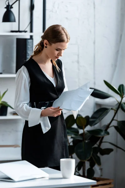 Femme d'affaires concentrée en tenue formelle détenant des documents sur le lieu de travail — Photo de stock