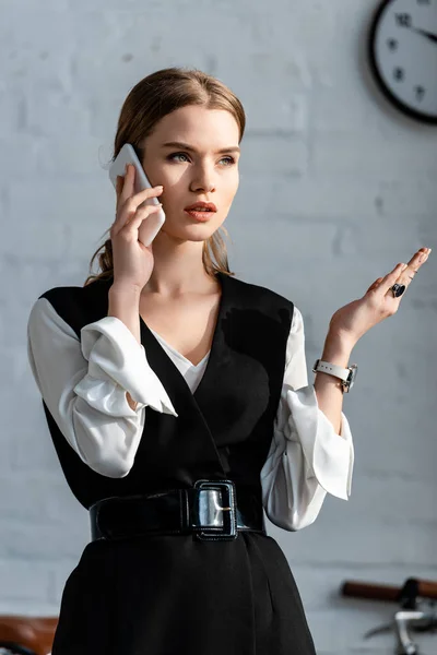 Beautiful businesswoman in formal wear gesturing and talking on smartphone in office — Stock Photo