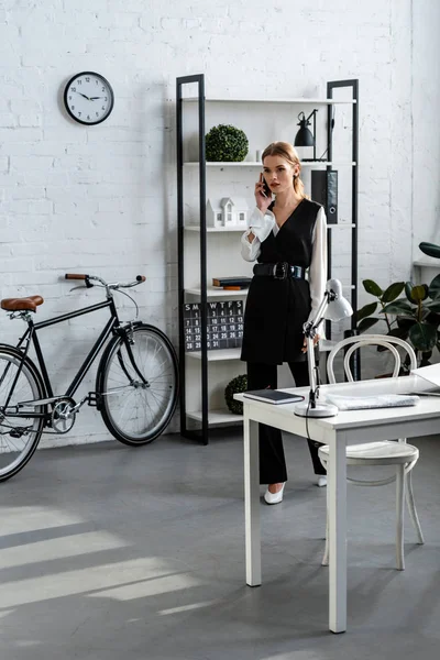Seriöse Geschäftsfrau in formeller Kleidung, die im modernen Büro mit dem Smartphone spricht — Stockfoto