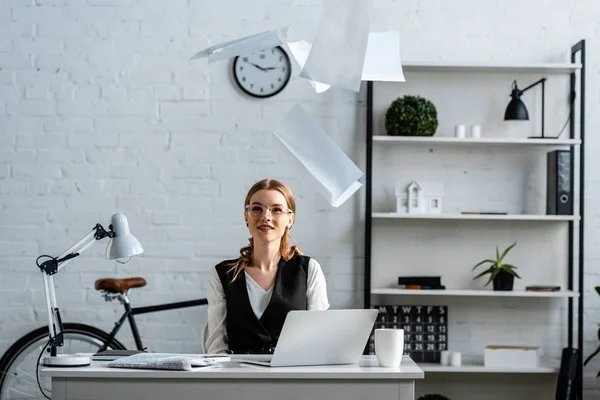 Mujer de negocios en ropa formal sentada en el escritorio y arrojando documentos al aire en el lugar de trabajo — Stock Photo