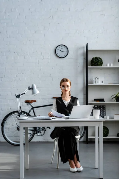 Femme d'affaires en tenue de cérémonie assise au bureau informatique avec des documents sur le lieu de travail — Photo de stock