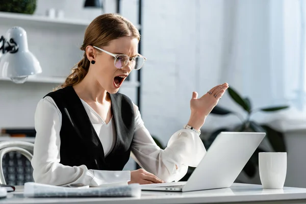 Shocked businesswoman in formal wear sitting at computer desk and gesturing with hands at workplace — Stock Photo