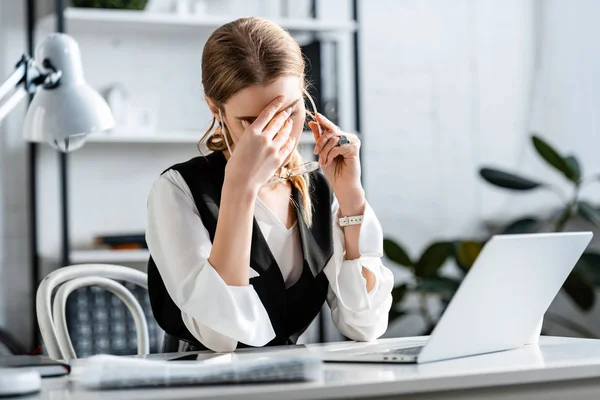 Selektiver Fokus einer Geschäftsfrau in formeller Kleidung, die am Computertisch sitzt, Stirn berührt und am Arbeitsplatz unter Kopfschmerzen leidet — Stockfoto