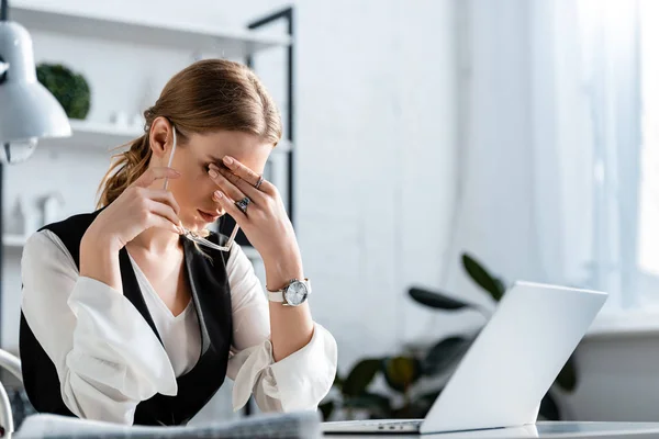 Donna d'affari in abito formale seduta alla scrivania del computer, che tocca la fronte e soffre di mal di testa sul posto di lavoro — Foto stock