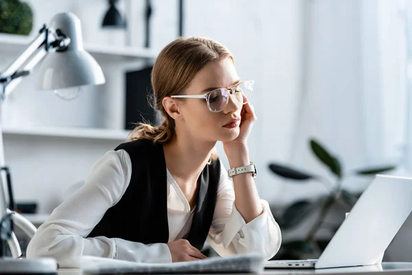 Belle femme d'affaires en tenue formelle et lunettes assis au bureau de l'ordinateur sur le lieu de travail — Photo de stock