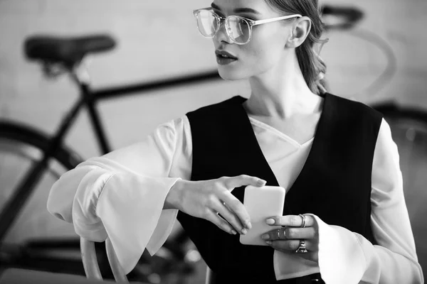 Черно-белое фото деловой женщины в формальной одежде с помощью смартфона на рабочем месте — стоковое фото
