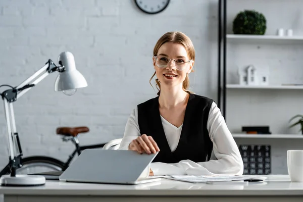 Schöne lächelnde Geschäftsfrau in formeller Kleidung, die am Computertisch am Arbeitsplatz sitzt — Stockfoto