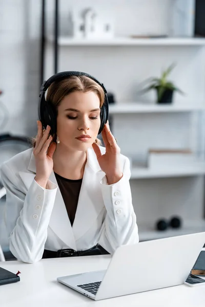Focused businesswoman in headphones and formal wear sitting at computer desk at workplace — Stock Photo