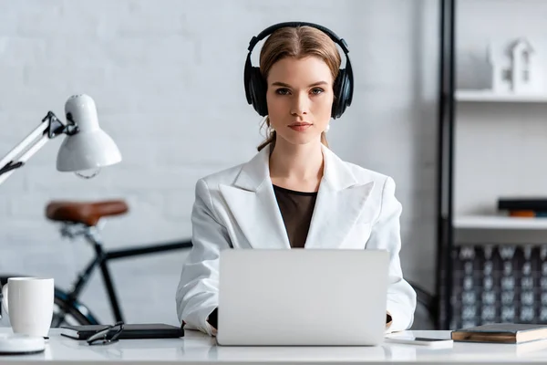 Серйозна бізнес-леді в навушниках сидить за комп'ютерним столом на робочому місці — стокове фото